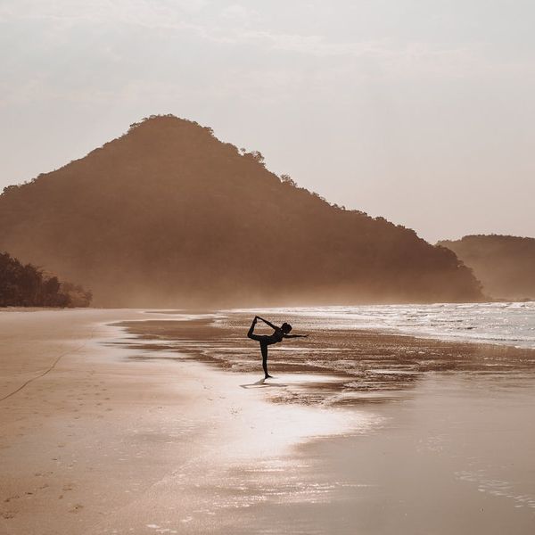 Person in a calm meditative pose overlooking a tranquil landscape at sunrise.