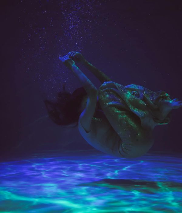 Woman performing a graceful yoga pose in a dark, atmospheric setting with neon blue light trails.